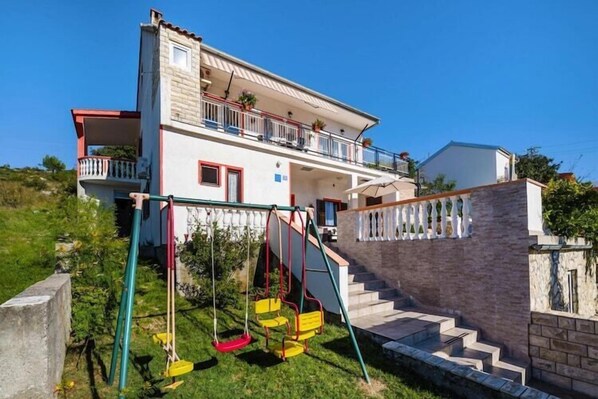 Una casa a due piani con un balcone, altalena e un muro in pietra.