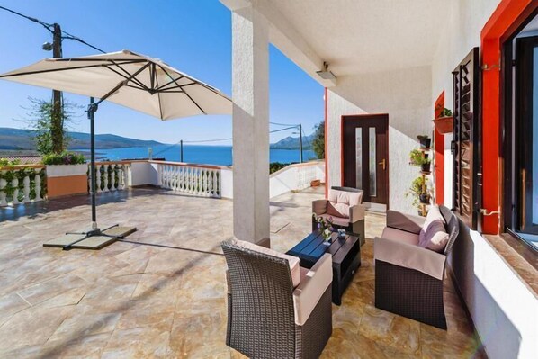 Une terrasse avec des meubles en osier, une table et un parasol.