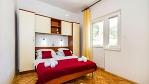 Un dormitori amb llit, sòl de fusta, finestra amb cortines i armari encastat.