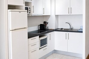 A kitchen with white cabinets, a black countertop, a built-in microwave, a stove, and a sink.