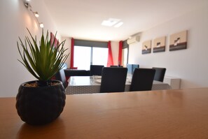Una habitación moderna con una mesa de madera, una planta en maceta, un comedor con sillas y una ventana con cortinas rojas.