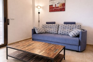 A room with a blue sofa, patterned cushions, a wooden coffee table, a floor lamp, and a piece of abstract art on the wall.