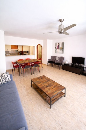 A modern living room with a dining area, a sofa, a coffee table, a TV, and a ceiling fan.