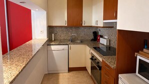 Eine kleine Küche mit Geschirrspüler, Backofen, Mikrowelle und einem roten Schrank.