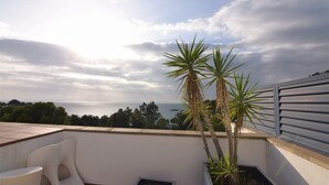 Terraço no telhado com vista para o mar, cadeiras brancas e duas plantas em vasos.