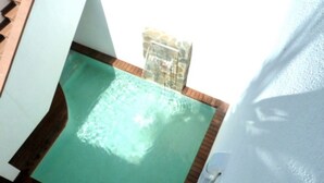 Área de piscina com deck de madeira e parede branca.