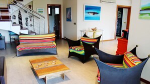 Uma sala de estar com uma mesa de centro de madeira, duas poltronas listradas, uma cadeira preta e um armário vermelho.