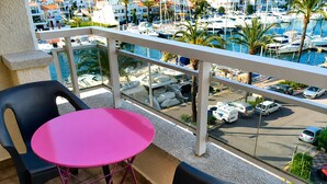 Ein Balkon mit einem rosafarbenen Tisch und zwei Stühlen, mit Blick auf einen Jachthafen mit Booten und einem Parkplatz.