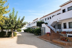 A row of white buildings with balconies, a gravel path, and potted plants.