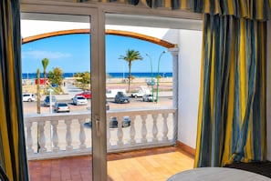A balcony with a view of the beach, parked cars, and palm trees.