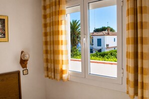 Una habitación con ventana, cortinas, una lámpara de pared e imagen en un marco.