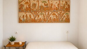 Ein Schlafzimmer mit einem großen Bett, einem kleinen Nachttisch mit Pflanze und Kerze sowie einer Wandteppich.