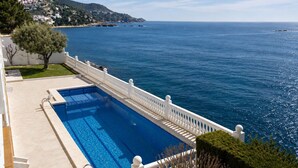 Ein Pool mit weißer Brüstung, freier Meerblick und ein Hügel mit Gebäuden im Hintergrund.