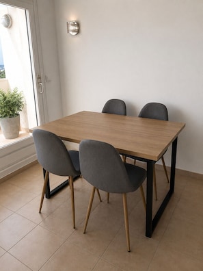 Een eettafel met vier stoelen, een potplant en een wandlamp.