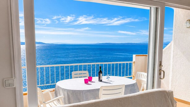 Ein Balkon mit Tisch für zwei Personen mit Blick auf ein Gewässer.