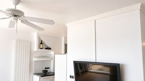 Eine moderne Küche mit weißen Schränken, einem eingebauten Backofen, einer Mikrowelle, einem Deckenventilator und einem flachbildfernseher an der Wand.