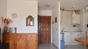 A kitchen with white cabinets, a wooden door, a blue trash bin, and a dining table. - 337-Nice apartment with view on the marina (Empuriabrava)