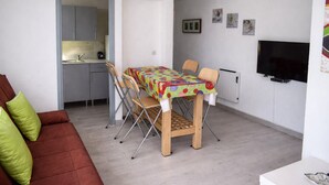 Een ruimtelijke woonkamer met een eettafel, stoelen, een bank, een televisie en een keukenhoek.