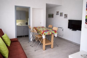 A compact living space with a dining table, chairs, a sofa, a TV, and a kitchen area.