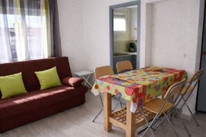 A room with a red sofa, a wooden table with a colorful tablecloth, and a chair.
