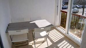 Een balkon met een tafel en stoelen, een uitzicht op geparkeerde auto's en gebouwen op de achtergrond.