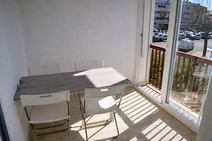 A balcony with a table and chairs, a view of parked cars, and buildings in the background.