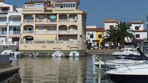 Ein mehrstöckiges Gebäude mit Balkonen, eine Marina mit Booten und eine Palme.