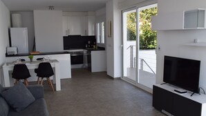 Eine moderne Wohnung mit Wohnzimmer, Essbereich, Küche und einem Balkon mit Fernseher.