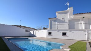 Ein moderner Poolbereich mit einem klaren, blauen Pool, einem weißen Gebäude mit einem geFliester Dach und einem gepflegten Rasen.