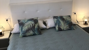 Ein Bett mit einem gepolsterten Kopfteil, zwei gemusterten Kissen und einer gesteppten Tagesdecke.