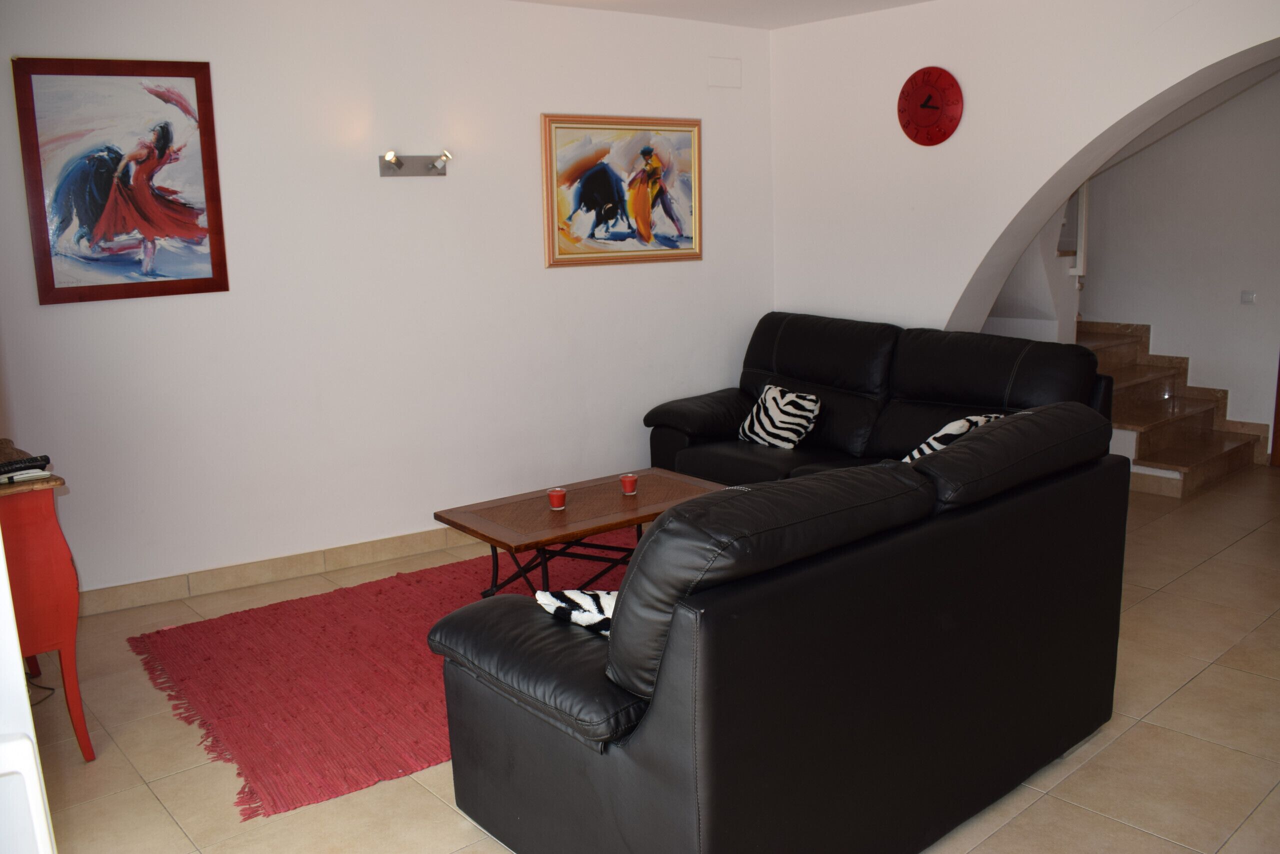 Uma sala de estar com um sofá de couro preto, uma mesa de centro de madeira e duas pinturas na parede.