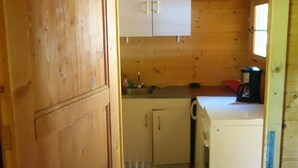 Innenansicht einer Holzhütte mit Küchenzeile, einschließlich Schränken, einem Spülbecken und einer Kaffeemaschine.
