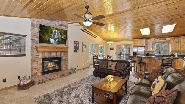 A spacious living room with a fireplace, leather sofas, a coffee table, and a dining area with a view. - Central Location at this Log Style Cabin! Open Concept Floor Plan! Luxury Cabin! Shuffleboard! BBQ! (Big Bear Lake)