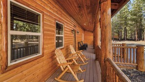 A wooden cabin with a porch, rocking chairs, and a view of the forest. - Central Location at this Log Style Cabin! Open Concept Floor Plan! Luxury Cabin! Shuffleboard! BBQ! (Big Bear Lake)