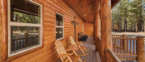 A wooden cabin with a porch, rocking chairs, and a view of the forest.