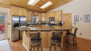 A kitchen with wooden cabinets, a stainless steel refrigerator, a microwave, and a large island with bar stools. - Central Location at this Log Style Cabin! Open Concept Floor Plan! Luxury Cabin! Shuffleboard! BBQ! (Big Bear Lake)
