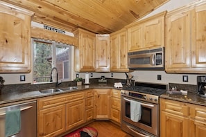 Une cuisine avec des meubles en bois, un évier en acier inoxydable, un four à micro-ondes, une cuisinière et une fenêtre donnant sur les arbres.