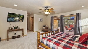 A bedroom with a bed, a ceiling fan, a TV, and a view of the outdoors. - Central Location at this Log Style Cabin! Open Concept Floor Plan! Luxury Cabin! Shuffleboard! BBQ! (Big Bear Lake)