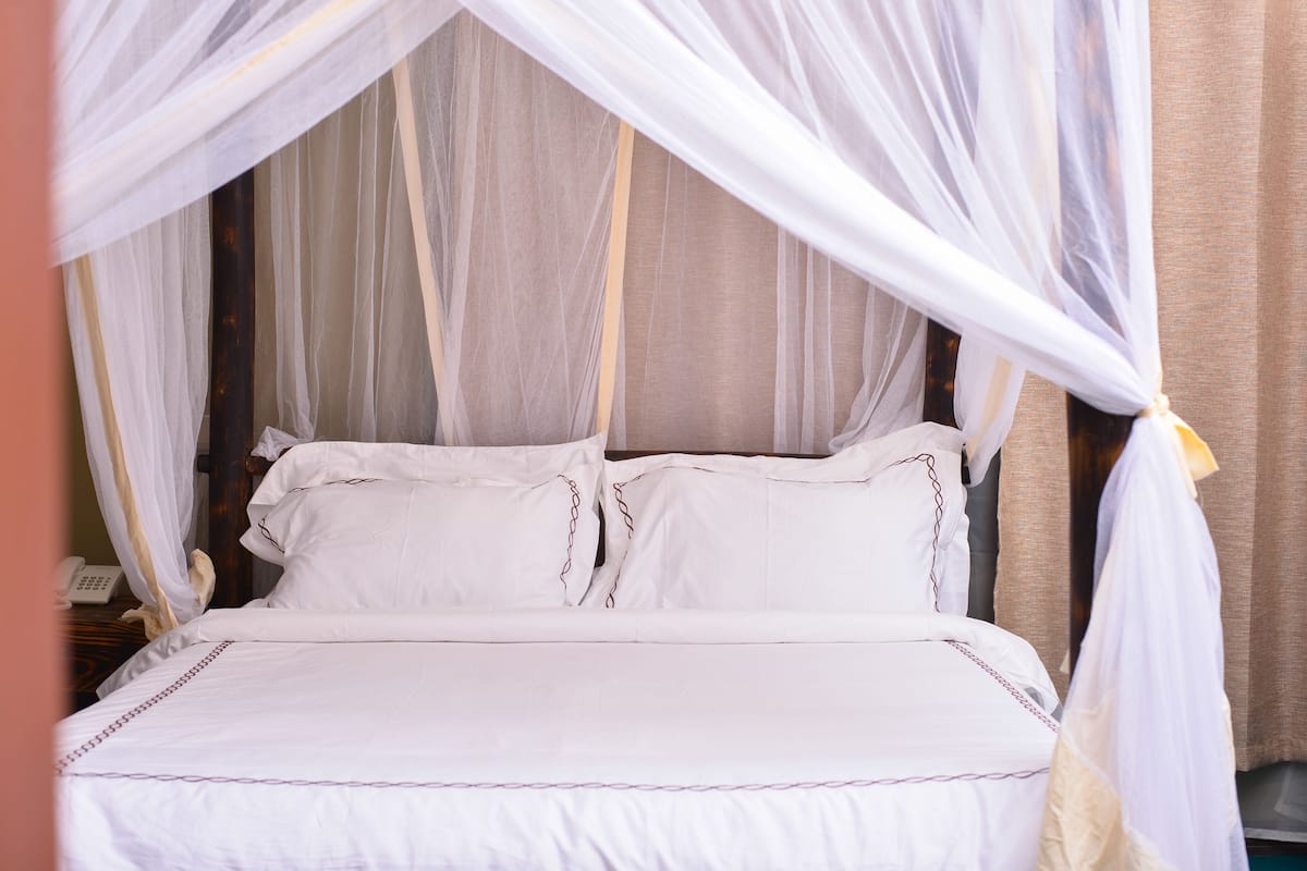 A bed with white bedding and a canopy, a bedside telephone, and a curtain.