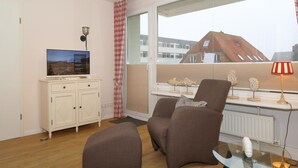 Ein modernes Wohnzimmer mit Fernseher, einem Glastisch und zwei braunen Sesseln.
