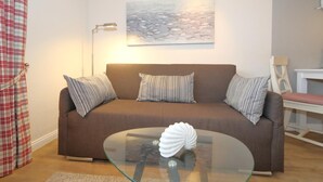 Ein Wohnzimmer mit braunem Sofa, gestreiften Kissen, einem Glastisch mit einer Dekoration und einem Gemälde an der Wand, sowie einer Lampe.