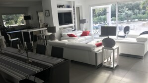 Ein modernes Wohnzimmer mit einem weißen Sofa, einem Essbereich mit einem gestreiften Tisch und einer Küche mit einem großen Fenster.