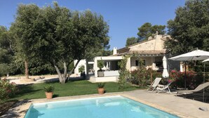 Ein Pool mit Sonnenterasse, ein überdachter Sitzbereich und ein Haus mit Steinverkleidung.
