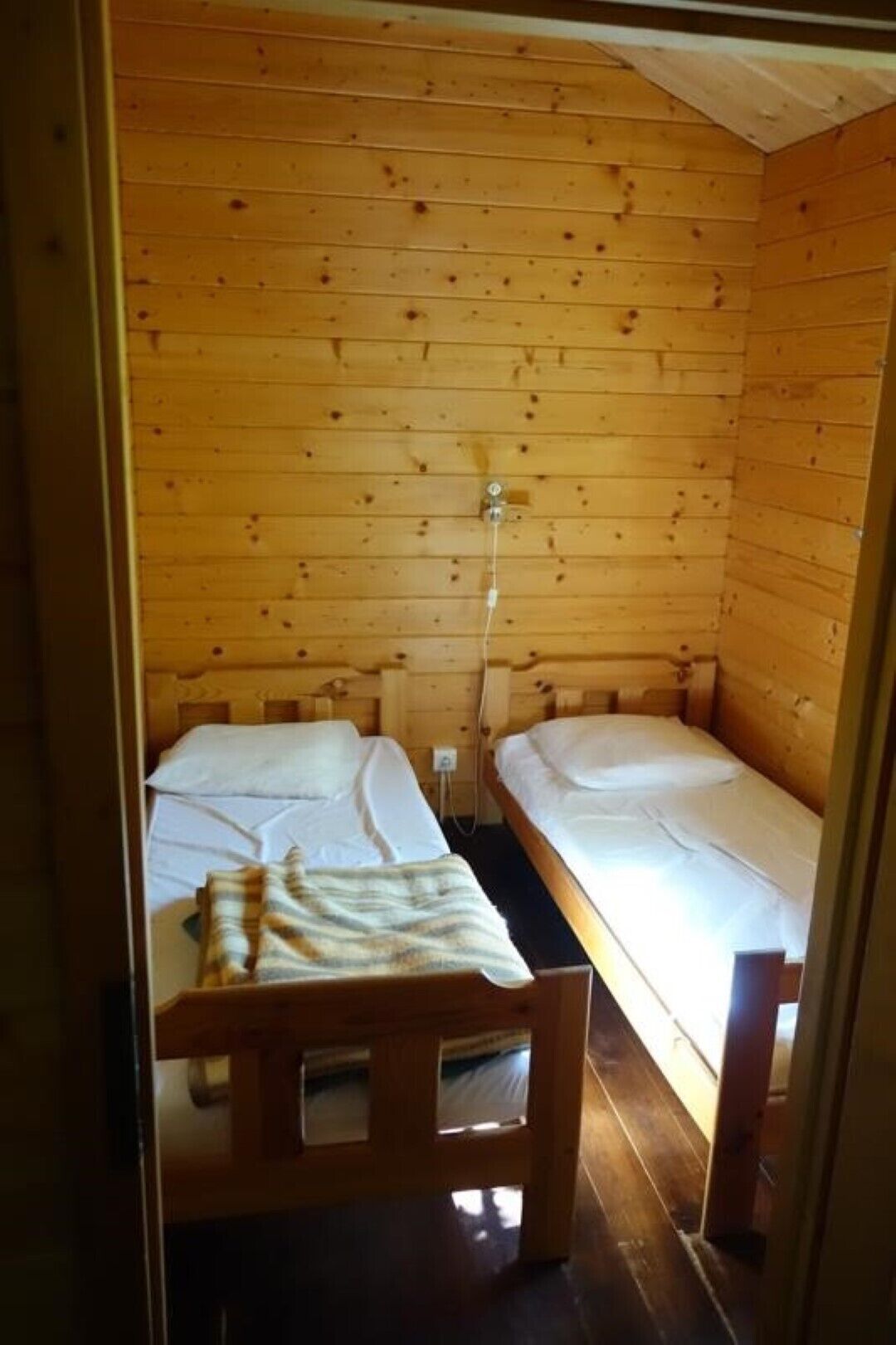 Pequeña habitación de cabaña de madera con dos camas individuales, un banco de madera y una lámpara de pared.