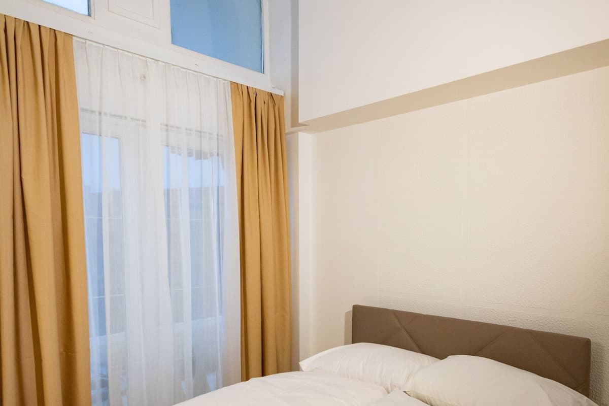Ein ordentlich bezogenes Bett mit weißen Leinen und Handtüchern, ein Holzboden und ein großes Fenster mit Vorhängen.
