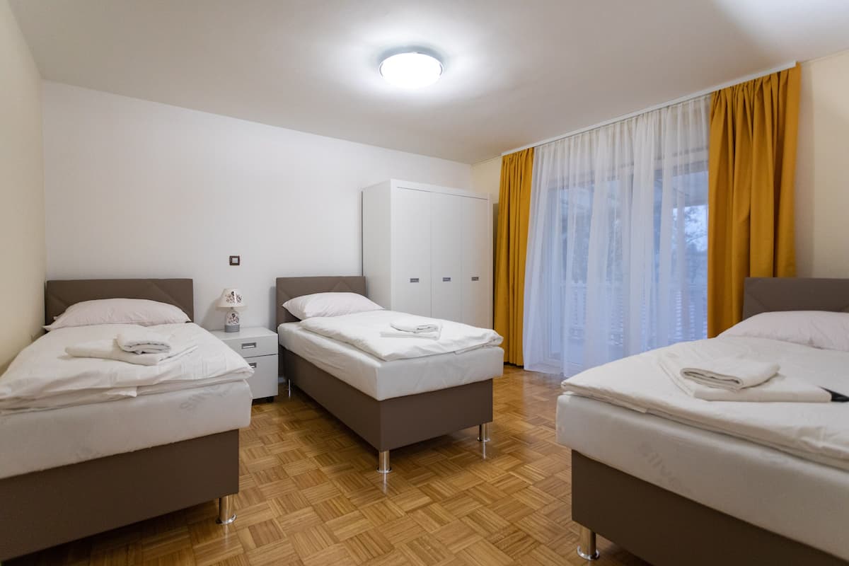 Ein Hotelzimmer mit drei Betten, einem Kleiderschrank und einem großen Fenster mit Vorhängen.