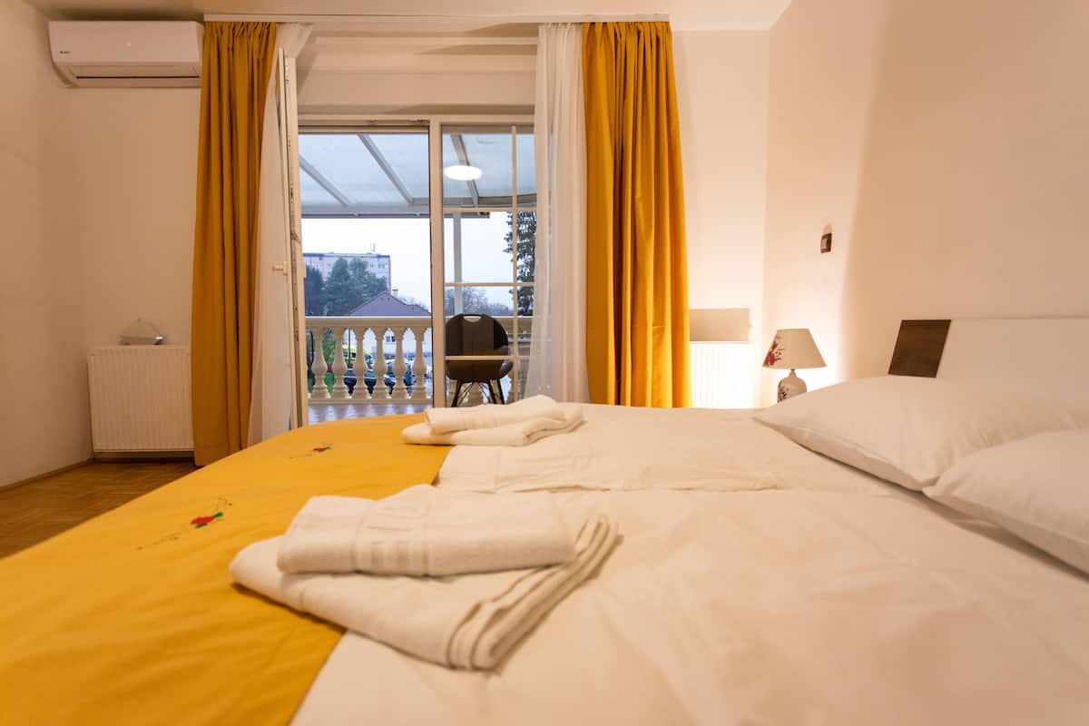 Ein Hotelzimmer mit einem großen Bett, einem Heizkörper, einem fenster mit Vorhängen, einem Sessel und einer Lampe.