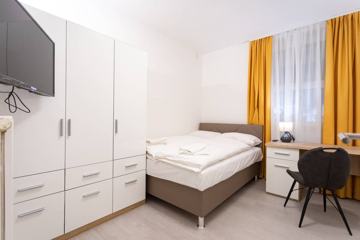 Ein Schlafzimmer mit Bett, Schreibtisch, Stuhl, Kleiderschrank und Fernseher.