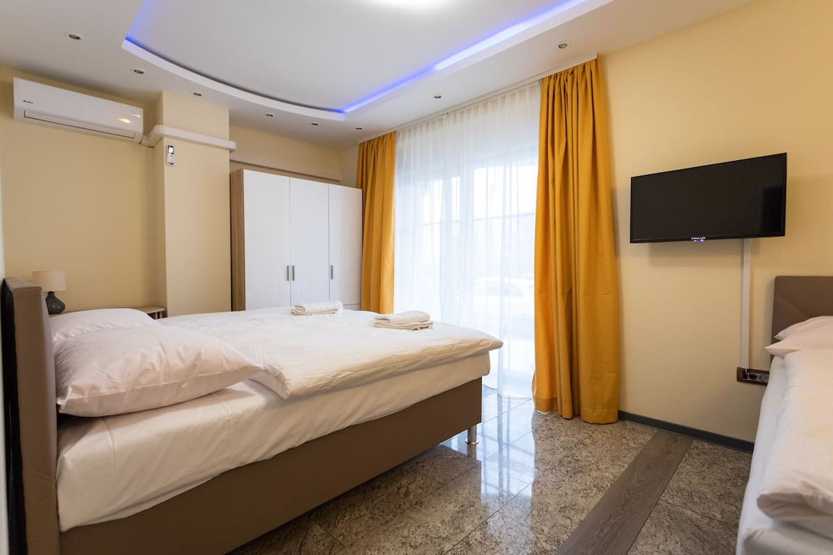 Ein Hotelzimmer mit einem großen Bett, einem flachbildfernseher an der Wand und einem Fenster mit gelben Vorhängen.