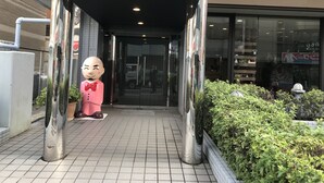 Een gebouwtoegang met een overdekte gangpad, een groot decoratief beeld en een potplant.